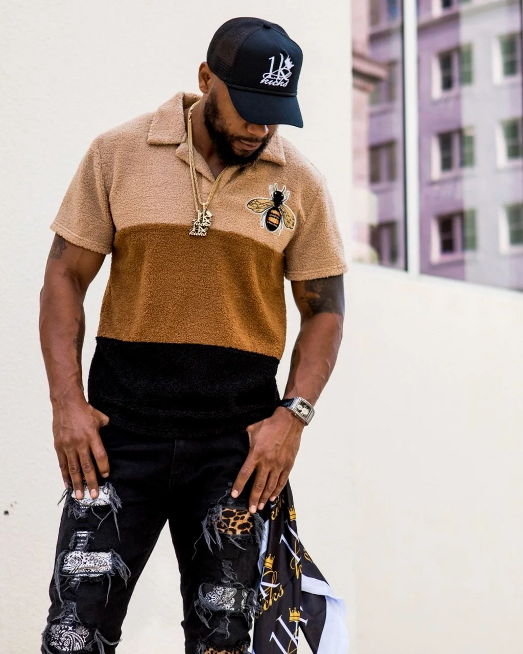 Model wearing the 1K Bee Chenille three tone streetwear polo with black jeans and a 1k Kicks hat