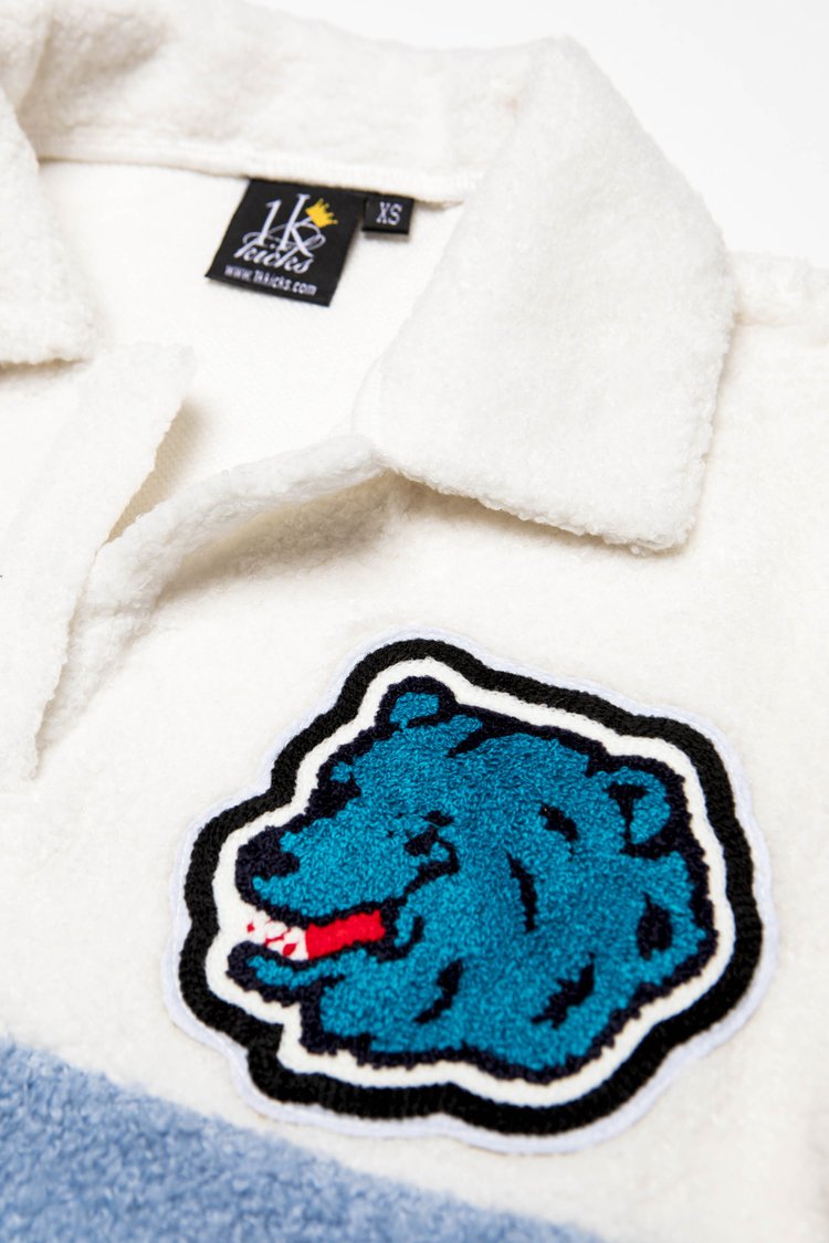 Close up of the grizzly bear patch and 1k Kicks label on the white chenille polo