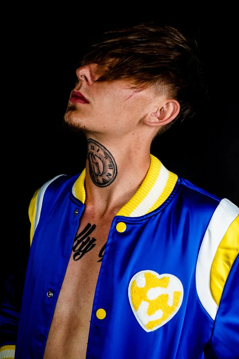 Close up of a model wearing the 1K Royal Love blue satin jacket with a yellow heart patch